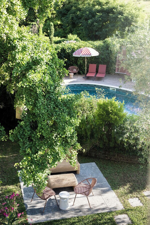 A poolside area with wicker furniture, a red and white striped umbrella, and lush greenery.