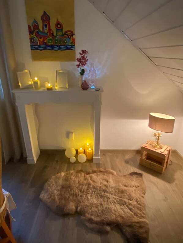 Um quarto acolhedor com lareira, velas, uma luminária e um tapete de pele no chão.