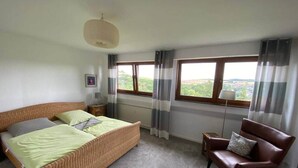 A bedroom with a bed, a chair, a lamp, and a window with curtains. - To complete (Burgbrohl)