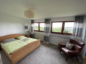 A bedroom with a bed, a chair, a lamp, and a window with curtains. - To complete (Burgbrohl)