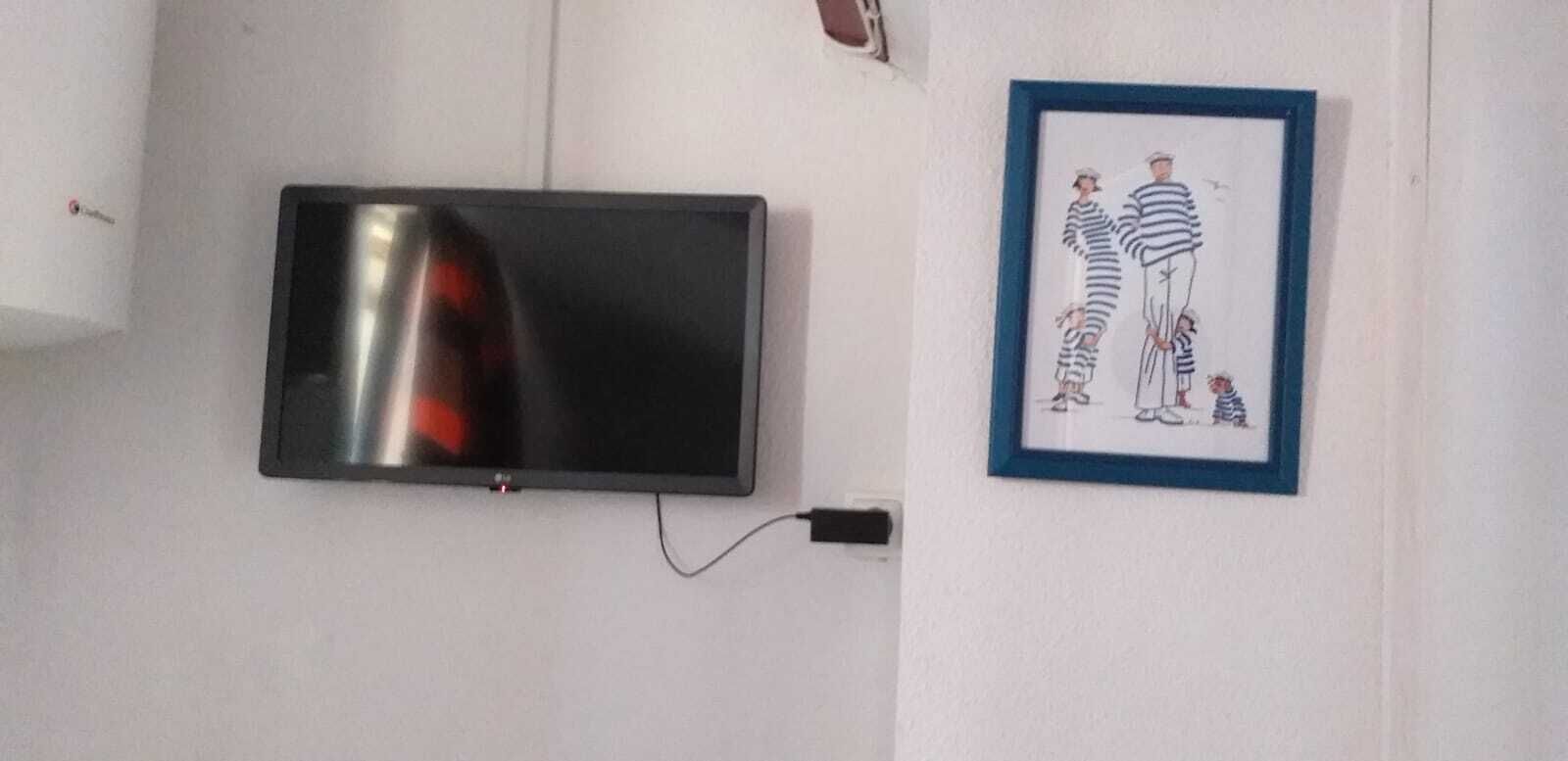 A flat-screen TV mounted on a wall, a framed picture of striped figures, and a visible electrical outlet.