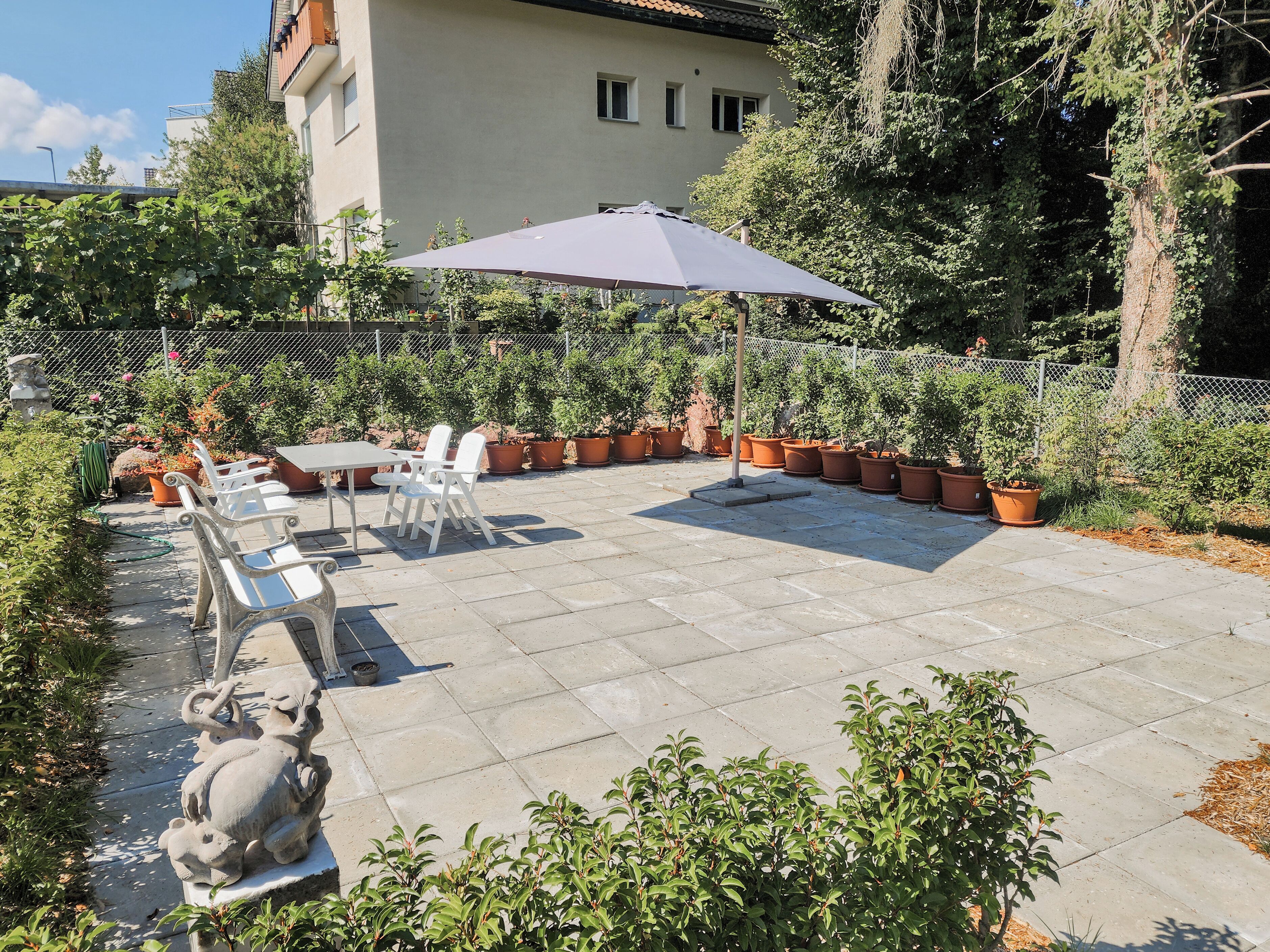 A patio with a table and chairs, surrounded by potted plants and a statue.