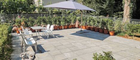 A patio with a table and chairs, surrounded by potted plants and a statue.