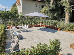 Une terrasse avec une table et des chaises, entourée de plantes en pot et d’une statue.