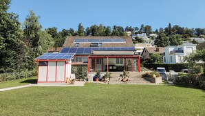 Una casa moderna con paneles solares, una puerta de vidrio con marco rojo y un césped cuidado.