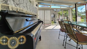 Un piano con diseños decorativos, una silla de mimbre y una mesa de cristal en un patio soleado con vistas a pájaros volando.