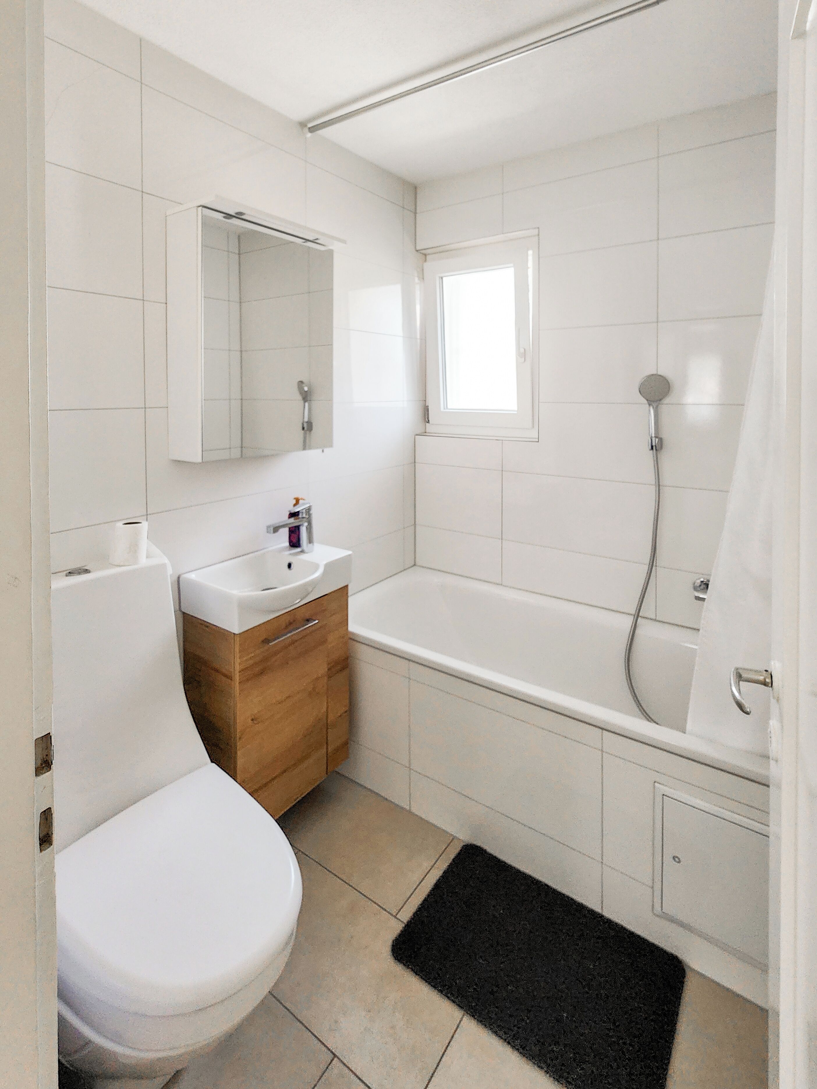 A bathroom with a toilet, sink, vanity, mirror, and bathtub.