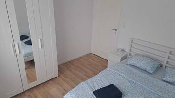 A bedroom with a wardrobe, a bed with patterned bedding, a bedside table, and a door.