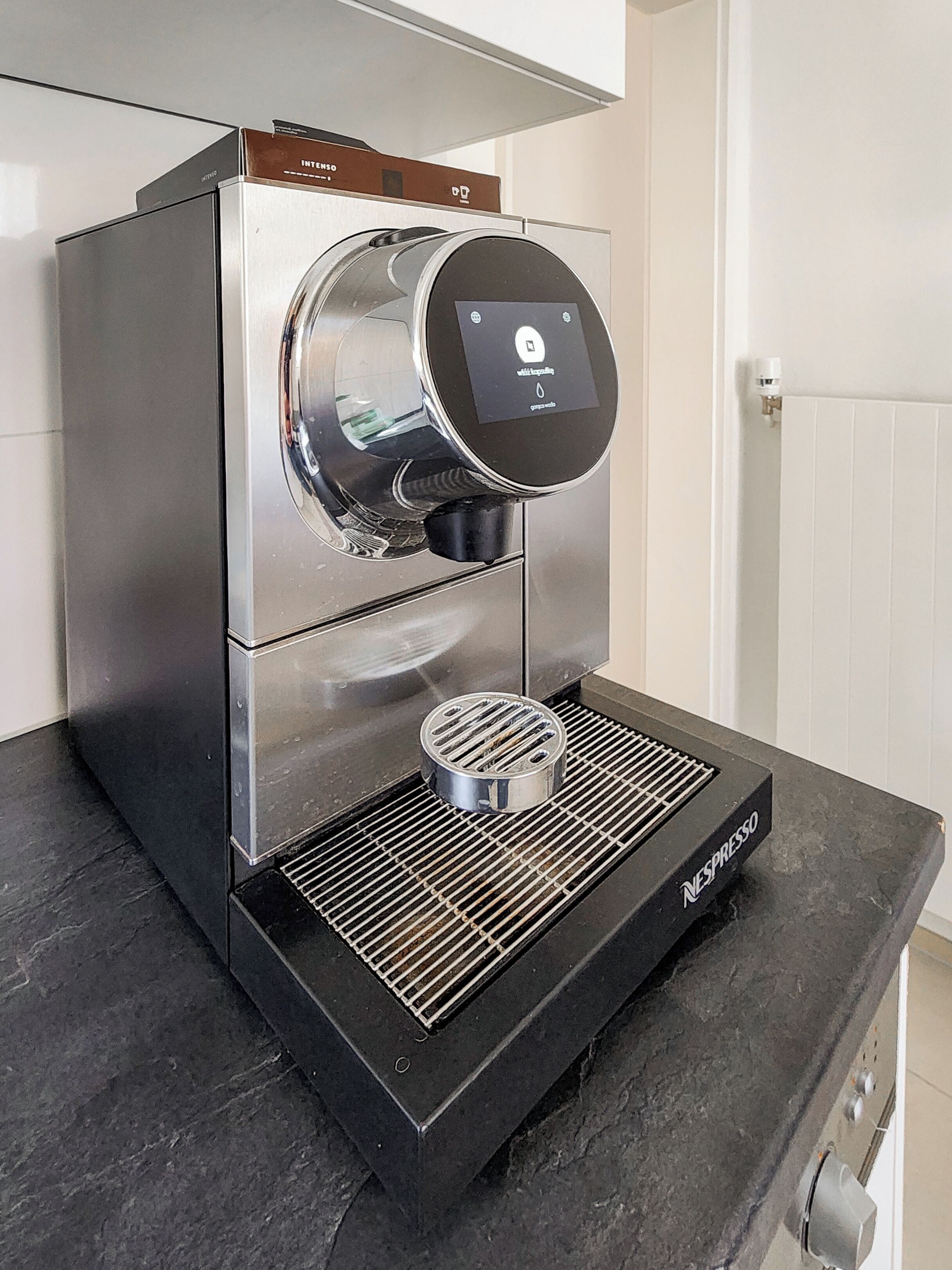 Une machine à café Nespresso dotée d’une interface numérique, d’un bac de récupération et d’un réservoir d’eau.