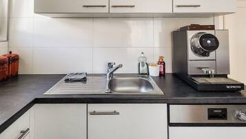 A modern kitchen with white cabinets, a stainless steel sink, and a built-in Nespresso coffee machine.