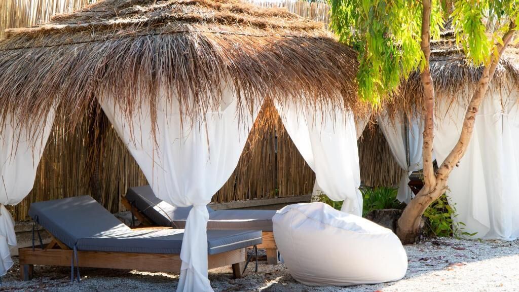 A thatched-roof structure with white drapes, two lounge chairs, and a bean bag chair.