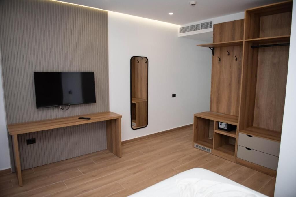 A modern bedroom with a TV, a mirror, a wooden wardrobe, and a bedside table.