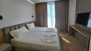 Une chambre d’hôtel avec deux lits, une télévision et une grande fenêtre avec des rideaux.