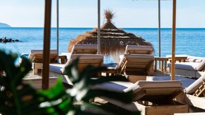 A beachside lounge area with wooden lounge chairs and a thatched roof structure. - White Hill Radhime (Orikum)