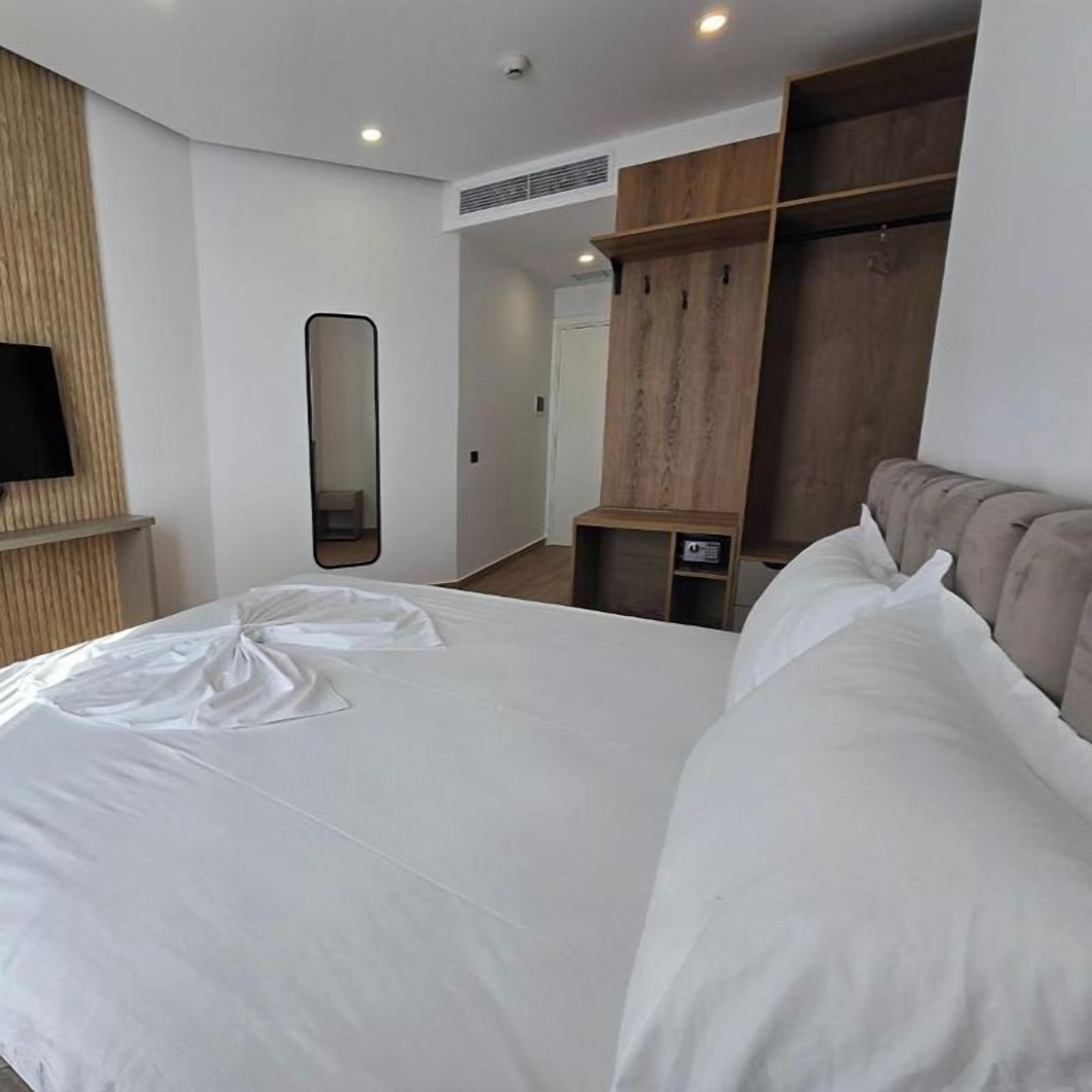 Een moderne hotelkamer met een groot bed, een houten garderobe, een spiegel en een televisie.