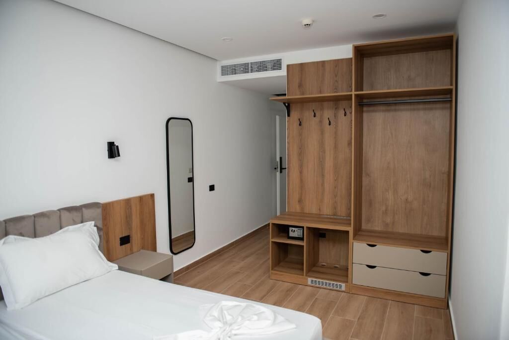 A bedroom with a bed, a wardrobe, a mirror, and a small shelf.