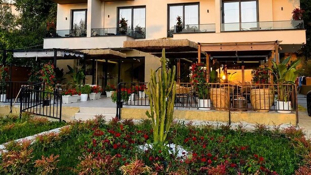 A multi-story hotel with balconies, a covered outdoor seating area, and a landscaped garden. - White Hill Radhime (Orikum)