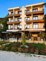A multi-story hotel with balconies, a covered outdoor seating area, and a landscaped garden.