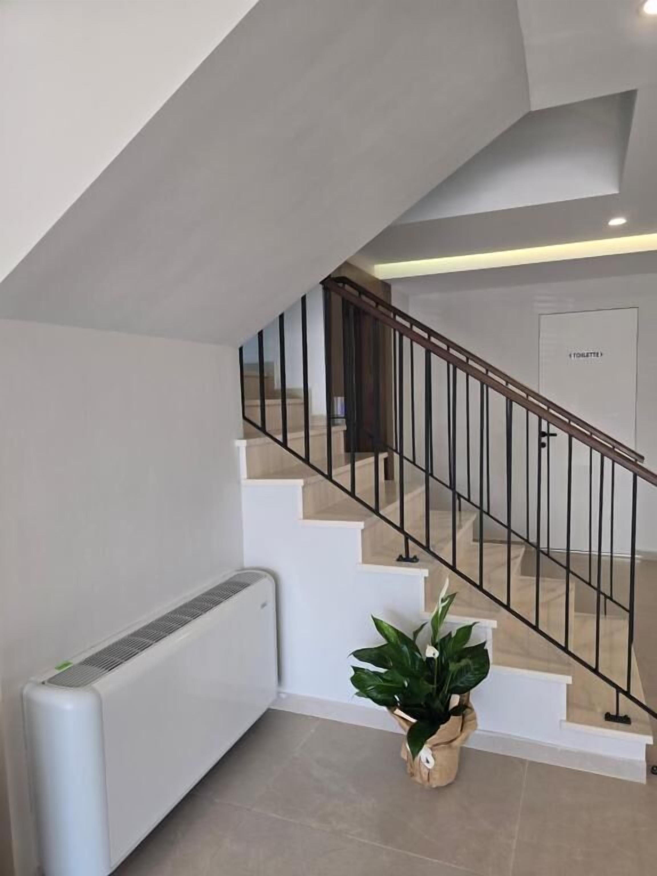 A modern staircase with a metal railing, a radiator, and a potted plant.