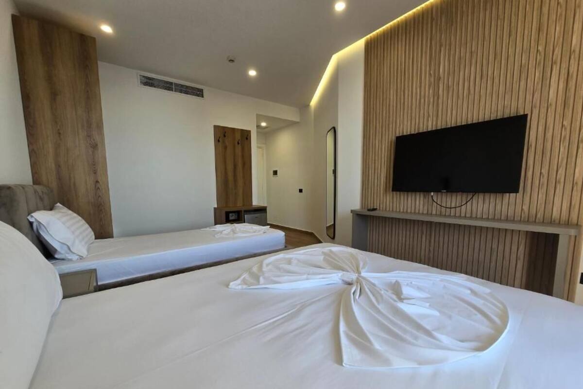 A hotel room with two beds, a TV mounted on the wall, and a wooden panel design on the wall.