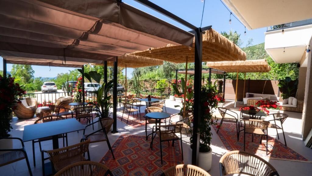An outdoor patio with tables and chairs, covered by canopies, and surrounded by potted plants and flowers.