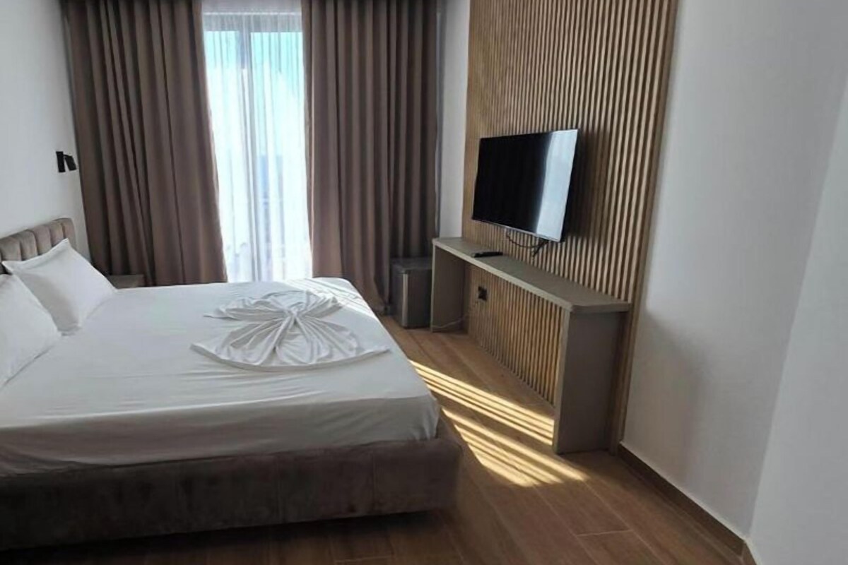 Une chambre d’hôtel avec un lit, un téléviseur fixé sur un panneau en bois et une fenêtre avec des rideaux.