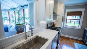 A modern kitchen with a stainless steel sink, white cabinetry, a stove, and a window with a view of greenery outside. - Game Room/Foosball/3BD/Families/Coffee Bar/Poker (Des Moines)