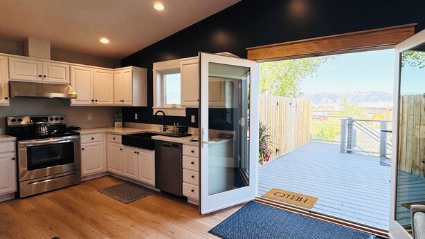 A modern kitchen with white cabinets, stainless steel appliances, and a sliding glass door leading to a deck with a 'HELLO' mat. - Entire rental unit. 5 guests. Large private deck. 2 beds. 1 sofa bed. 1 bath. (Belgrade)