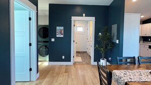 A modern kitchen with white cabinets, a dining table with chairs, and a hallway leading to a laundry room. - Entire rental unit. 5 guests. Large private deck. 2 beds. 1 sofa bed. 1 bath. (Belgrade)