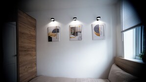 Ein Schlafzimmer mit einem Holzschrank, einem Bett mit einer beigefarbenen Bettdecke und drei an der Wand befestigten Kunstwerken.