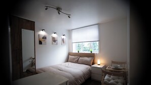 Ein Schlafzimmer mit Bett, Nachttisch, Lampe und einem Fenster mit Jalousien.