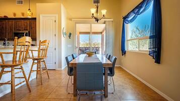 A dining area with a wooden table and chairs, a chandelier, and a view through a window with blue curtains.