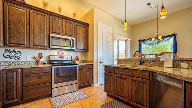 A kitchen with wooden cabinets, stainless steel appliances, granite countertops, and a patterned rug.