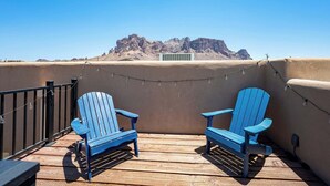 A balcony with two blue Adirondack chairs, a string of lights, and a view of a mountain range.