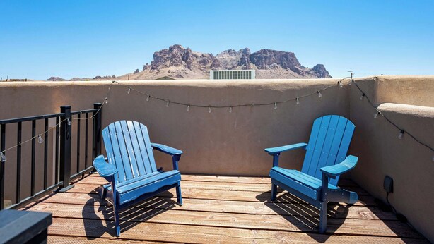 Een balkon met twee blauwe Adirondack-stoelen, een lichtslingering en uitzicht op een bergketen.