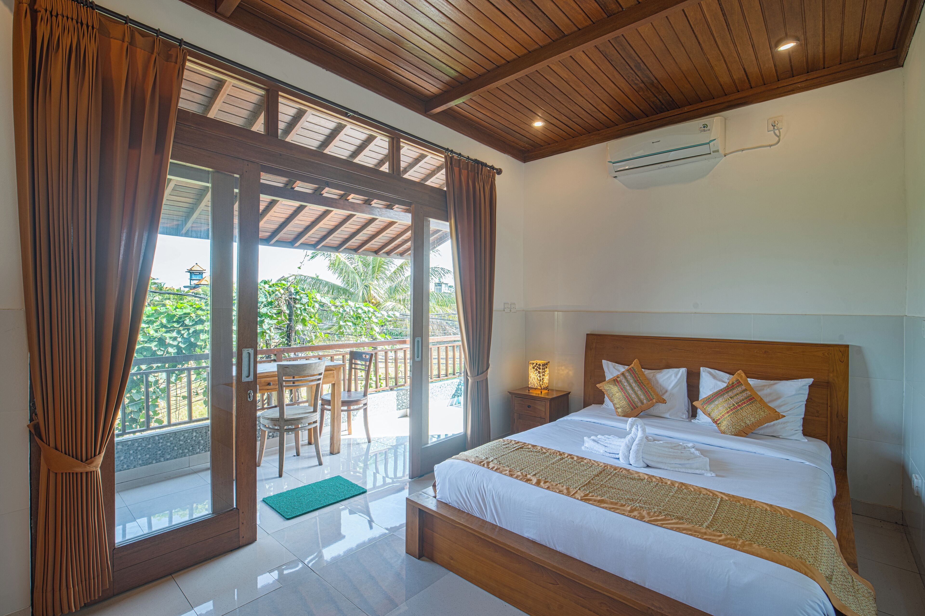 A bedroom with a large bed, wooden headboard, and a view of a balcony with a table and chairs.