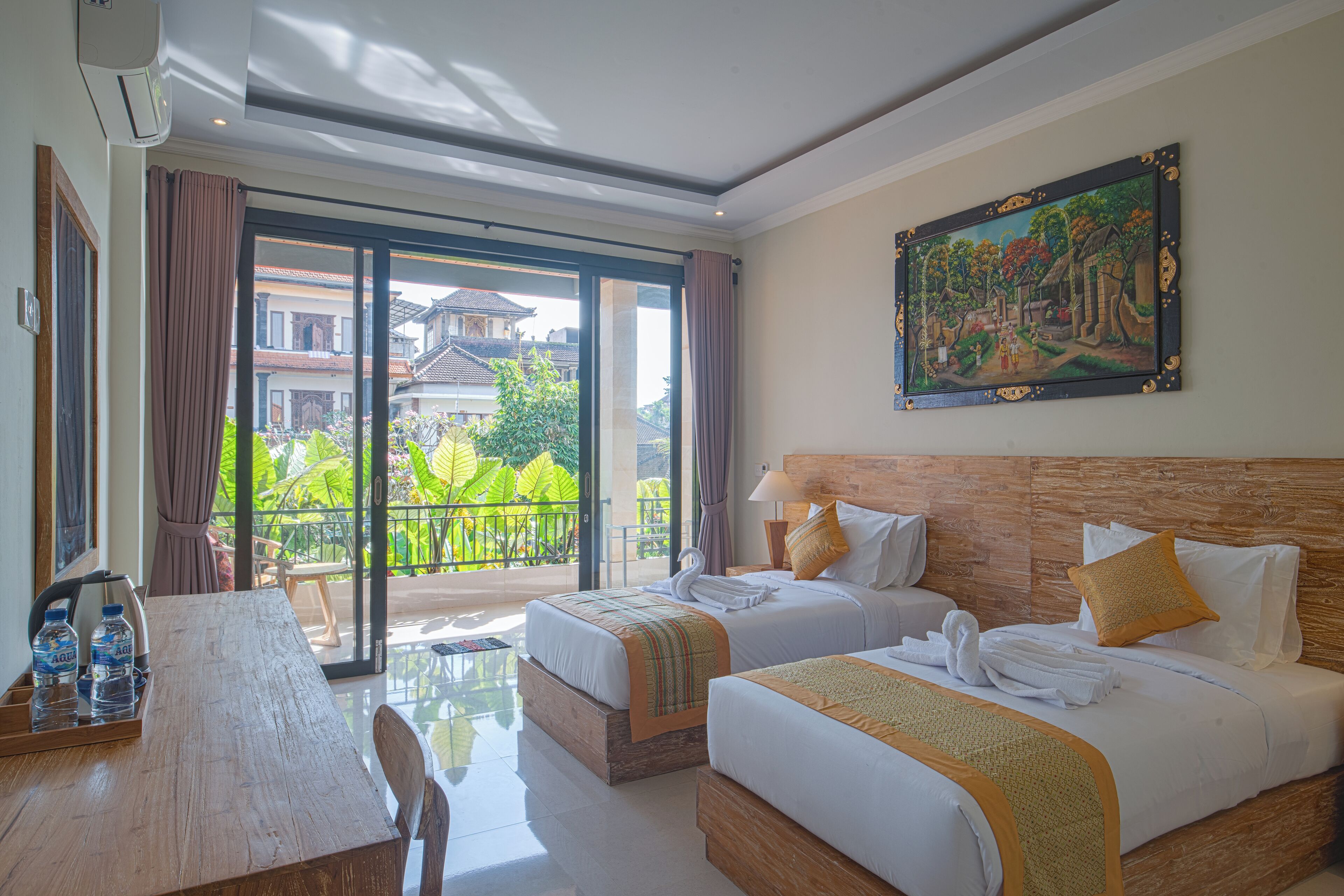 A hotel room with two beds, a dining table, and a balcony with a view of the surrounding area.