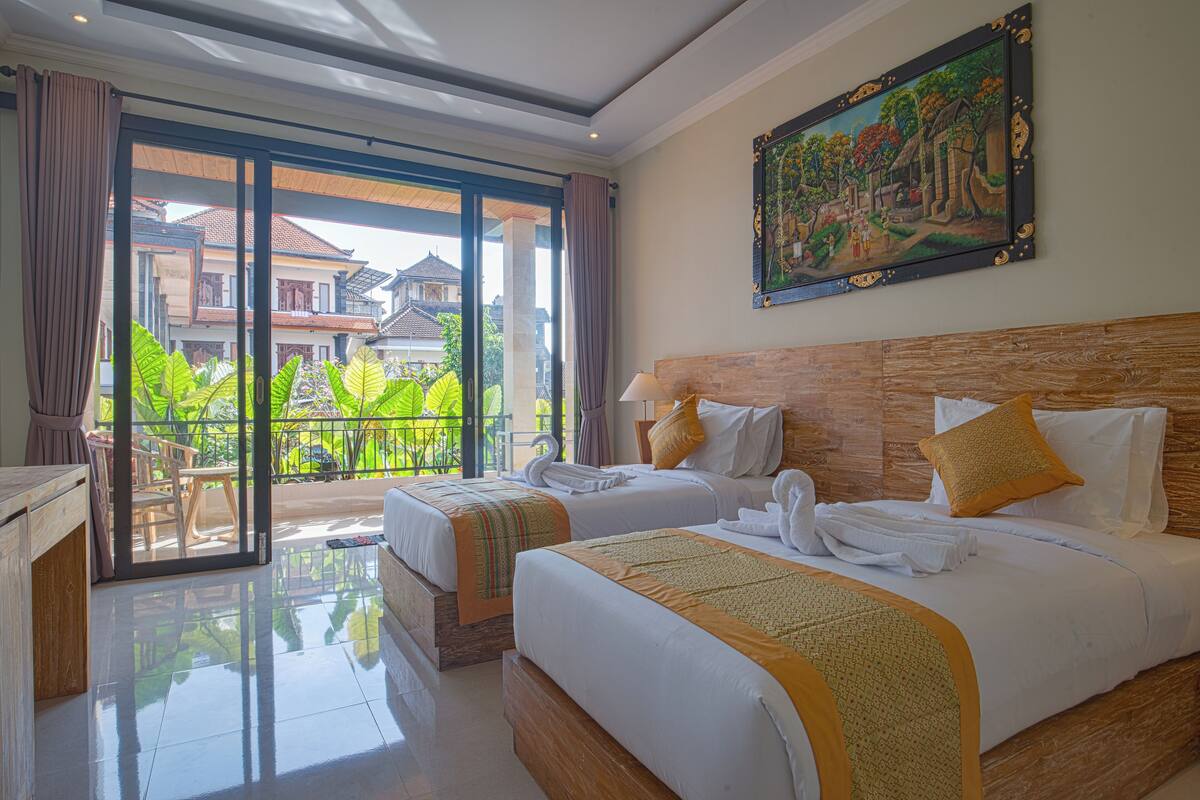 A hotel room with two beds, a balcony with a view of houses, and a painting on the wall.