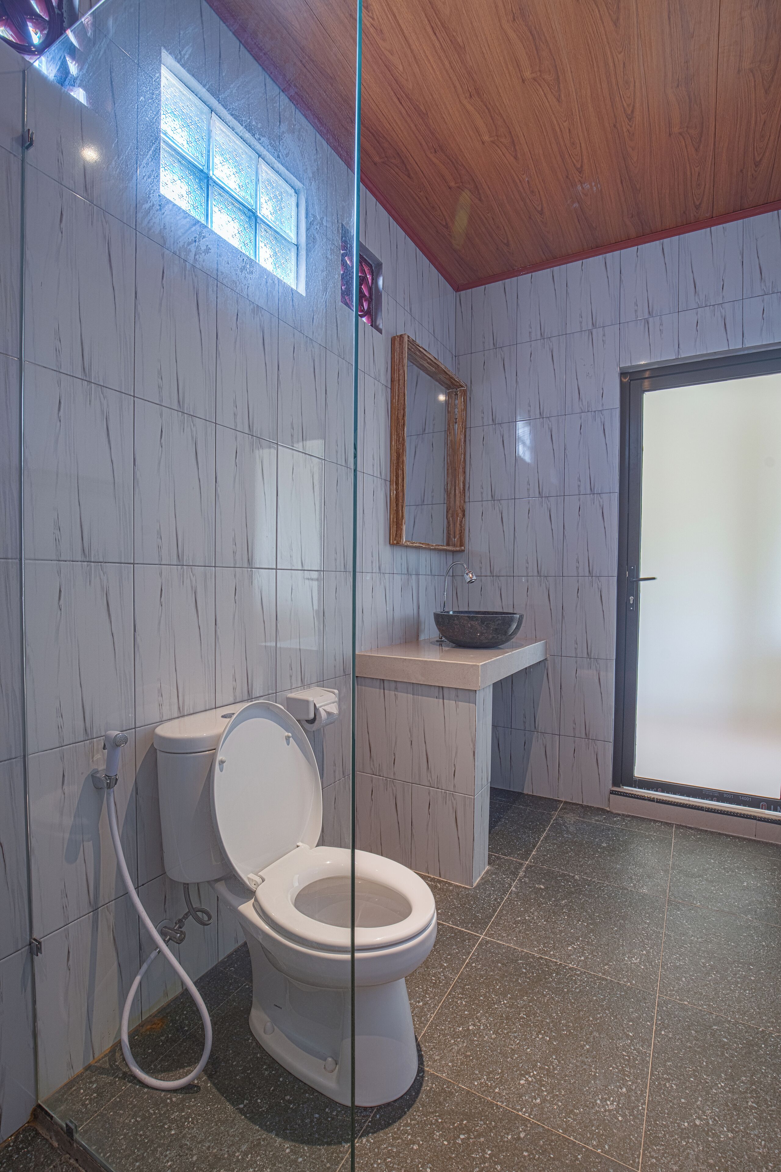 A modern bathroom with a white toilet, a vessel sink, and a wooden ceiling.