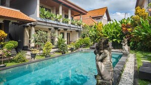 A swimming pool with a statue in the center, surrounded by lush greenery and a building with a tiled roof. - Darsa House Ubud (Ubud)