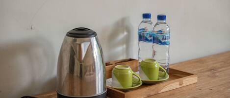 Una tetera eléctrica de acero inoxidable, dos tazas verdes y dos botellas de agua sobre una bandeja de madera.