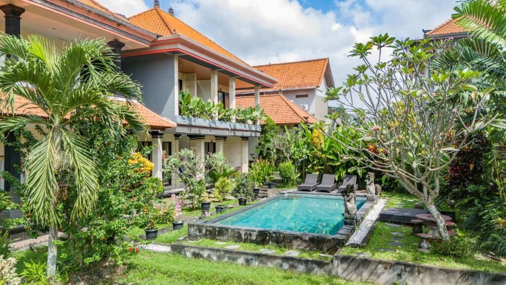 A residential property with a swimming pool, lush greenery, and a tiled roof.
