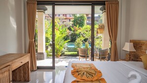 A hotel room with a bed, a wooden nightstand, a lamp, and a view of a pool and greenery outside. - Darsa House Ubud (Ubud)