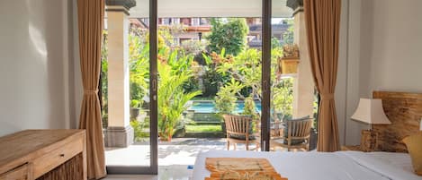 Habitación de hotel con una cama, una mesita de noche de madera, una lámpara y vistas a una piscina y zonas verdes.