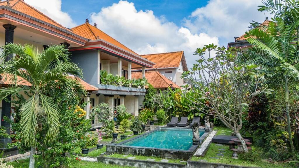 A two-story house with a swimming pool surrounded by lush greenery and palm trees.