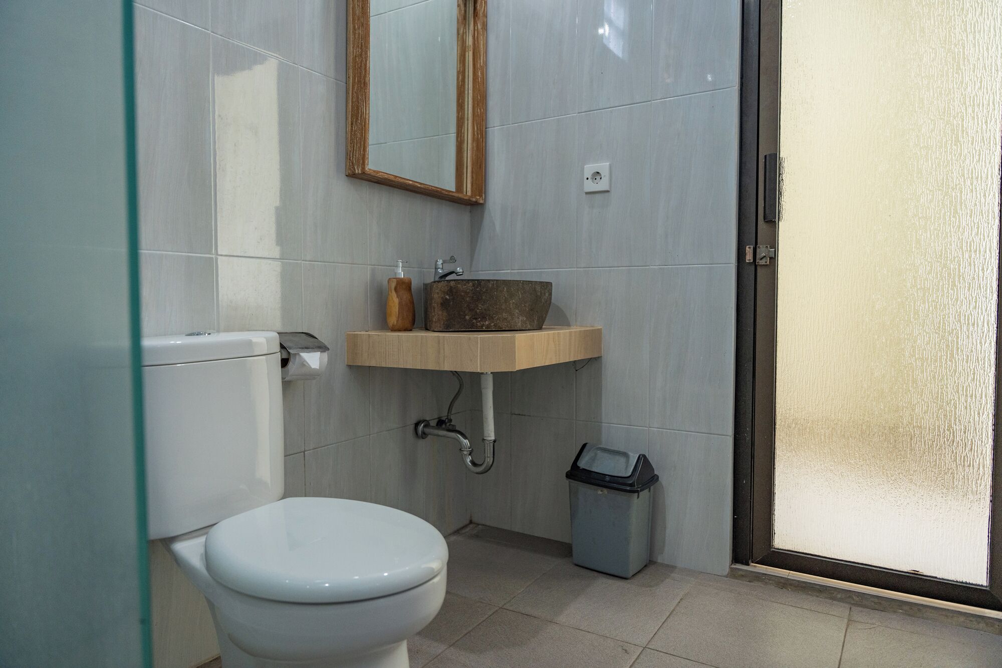 A bathroom with a toilet, a sink with a wooden countertop, a mirror, and a trash bin.