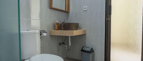 A bathroom with a toilet, a sink with a wooden countertop, a mirror, and a trash bin.