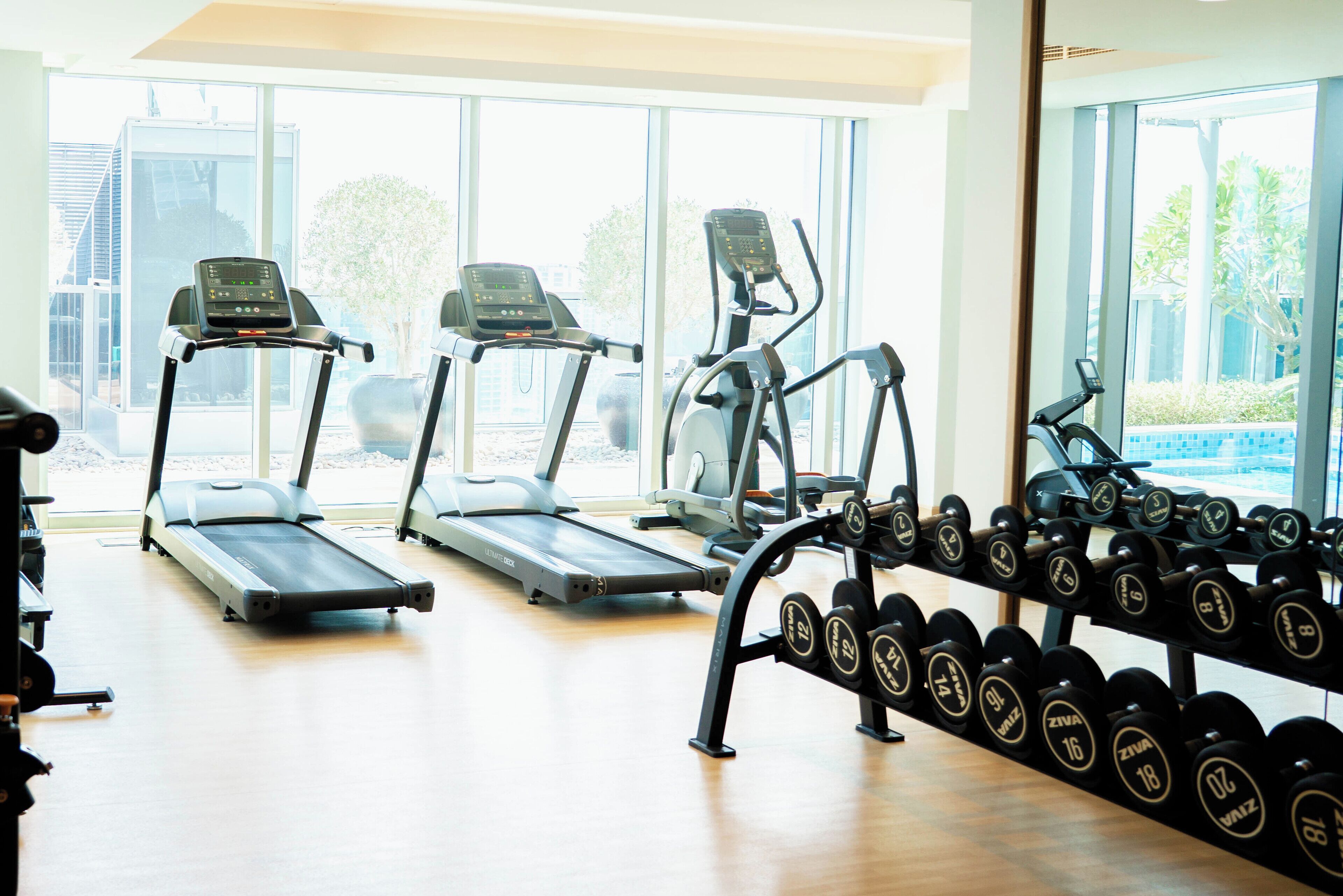 Ein Fitnessraum mit Laufbändern, Crosstrainern und einer Hantelbank.