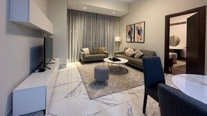 A modern living room with a flat-screen TV, two sofas, a coffee table, and a dining area with a table and chairs. - Modern 1BR in J One Pool & Gym (Dubai)