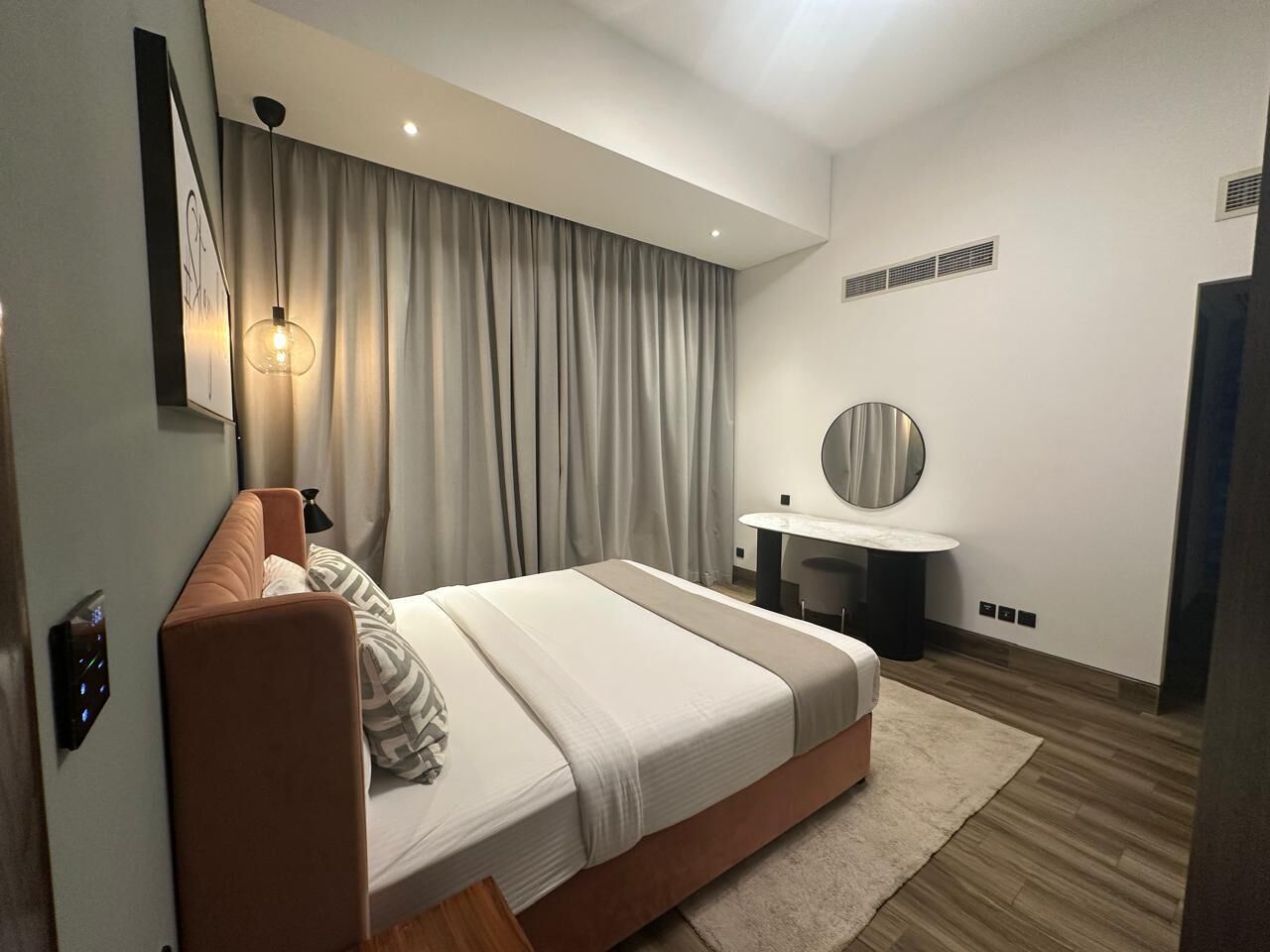 A modern bedroom with a bed, bedside table, and a round mirror.